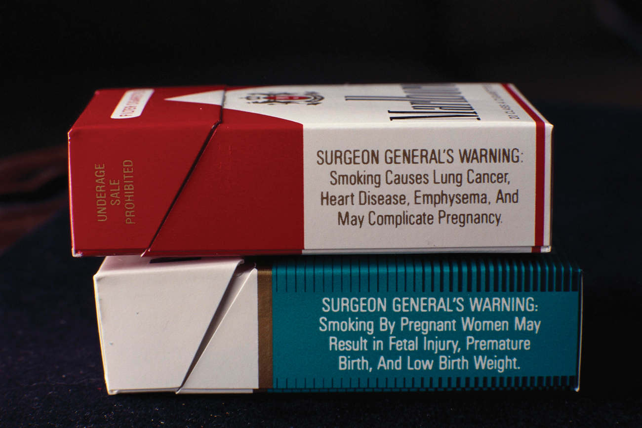 Image with the heading, “Surgeon general’s warnings”, showing side view of two cigarette packs. Cigarette pack on top shows the warning as, “Surgeon General’s Warning: Smoking causes lung cancer, heart disease, emphysema, and May complicate pregnancy”. The lower cigarette pack shows the warning as, “Surgeon General’s Warning: Smoking by pregnant women may result in fetal inquiry, premature birth, and low birth weight.”