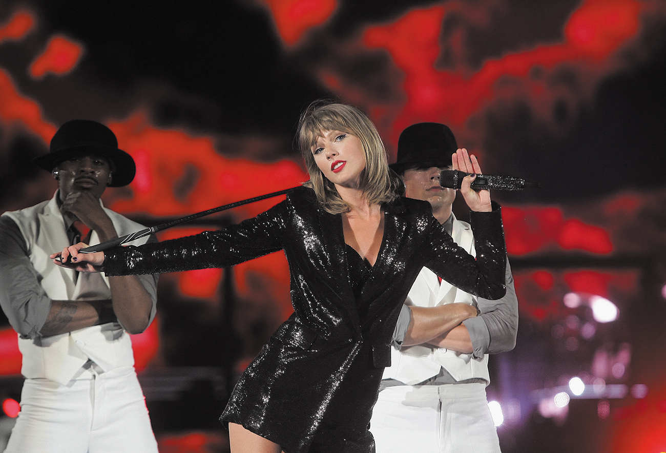 Image shows Talor Swift performing, with some background singers/dancers in the background.