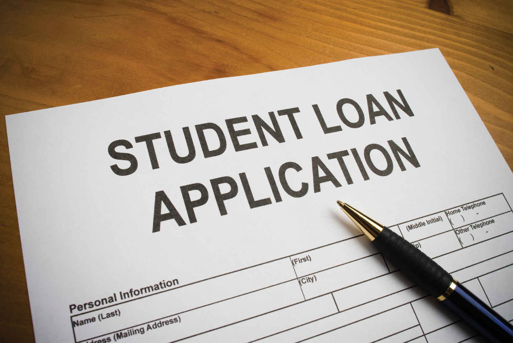 An image of an unfilled student loan application form along with a pen on it. It depicts the columns of personal information that requires to fill in a student’s name (last, first and middle), Address, city, zip code, home and other phone numbers.